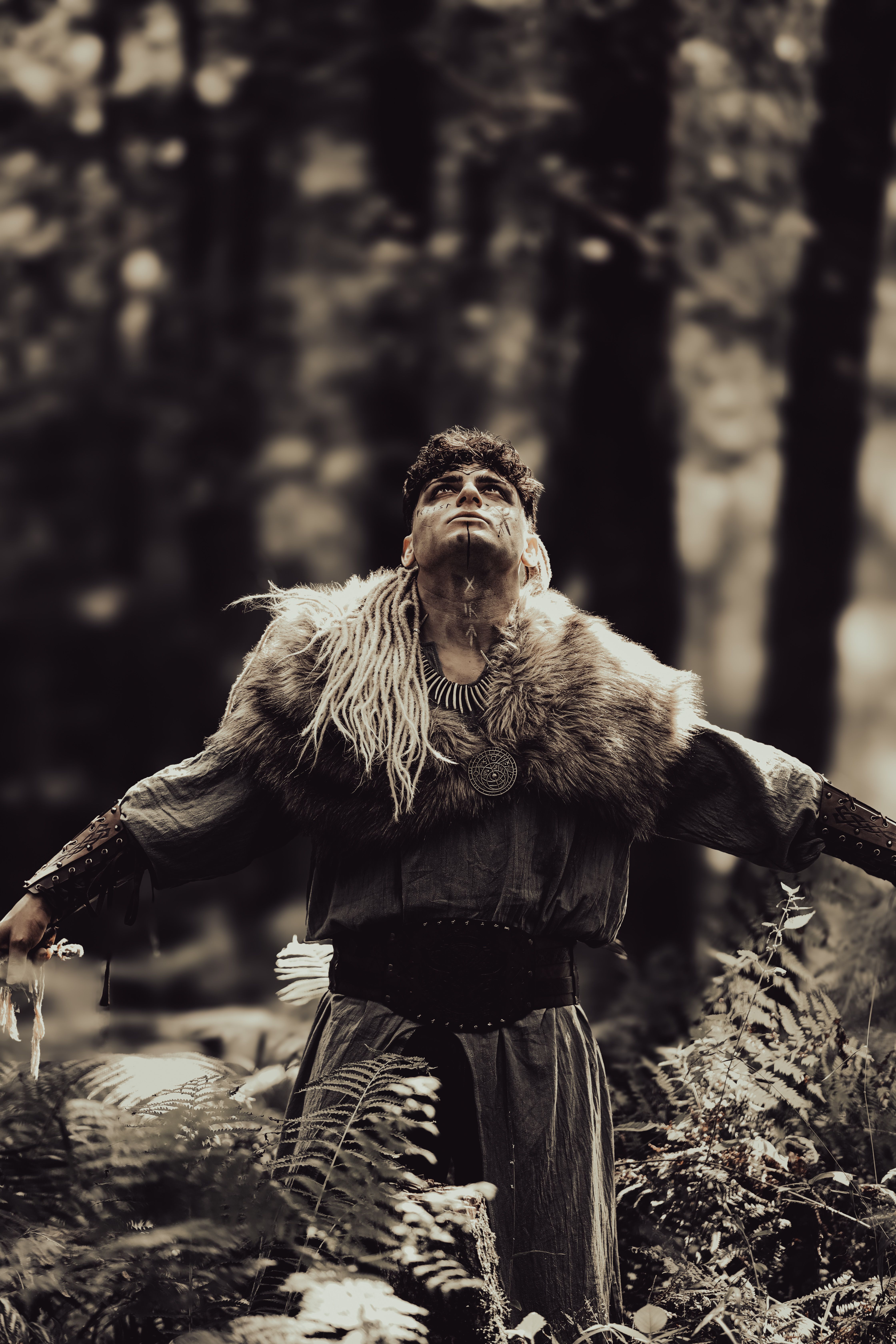 Viking warrior in traditional attire stands in an ancient forest, evoking a historical and mystical atmosphere.