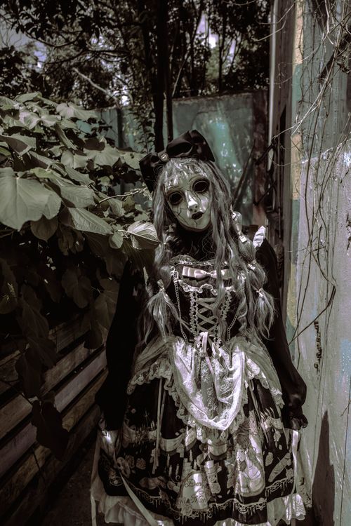 Free Eerie figure in doll costume stands in dimly lit alley, perfect for Halloween themes. Stock Photo