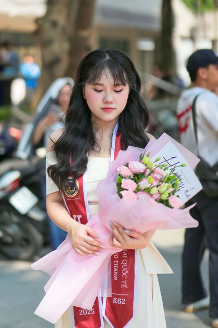 A young woman in a graduation gown holding flowers, celebrating her graduation day.