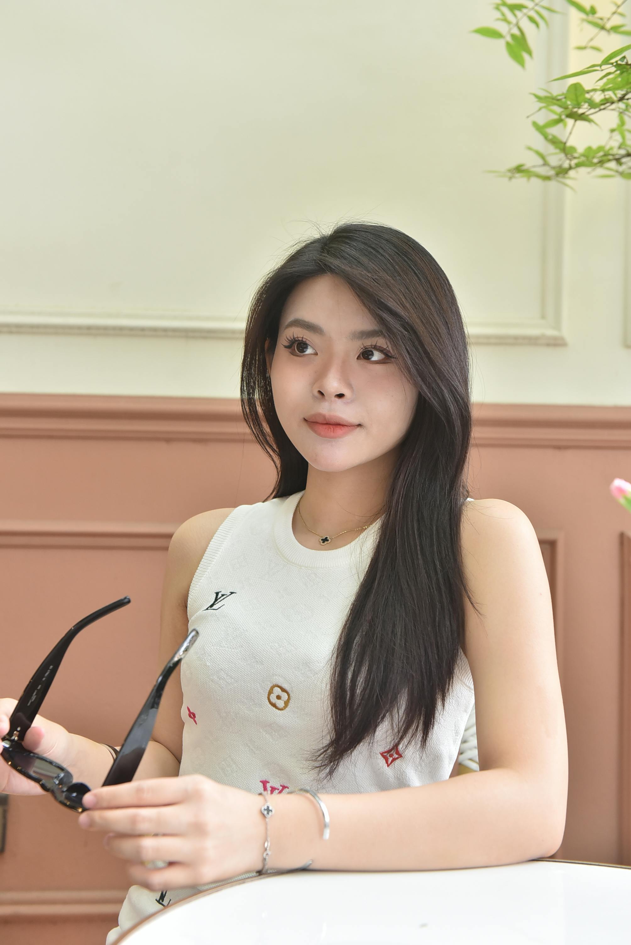 Ilmainen Nuori nainen istuu sisätiloissa aurinkolasit kädessään, eleganssia ja ryhtiä huokuen. Kuvapankkikuva