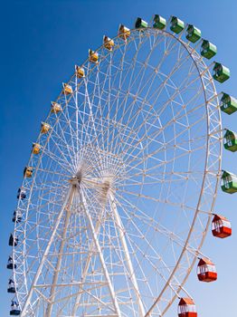 Vibrant Ferris wheel silhouetted against a clear blue sky in Bosteri, Kyrgyzstan.