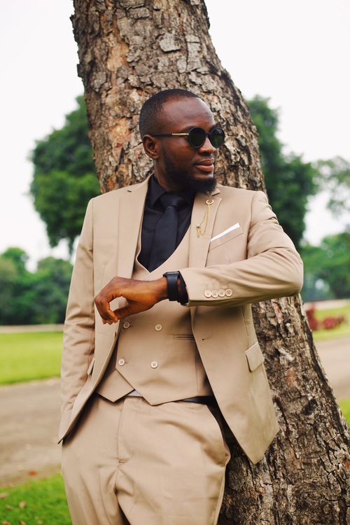 Free Elegant man in tan suit and sunglasses leans against a tree, showcasing modern fashion outdoors. Stock Photo