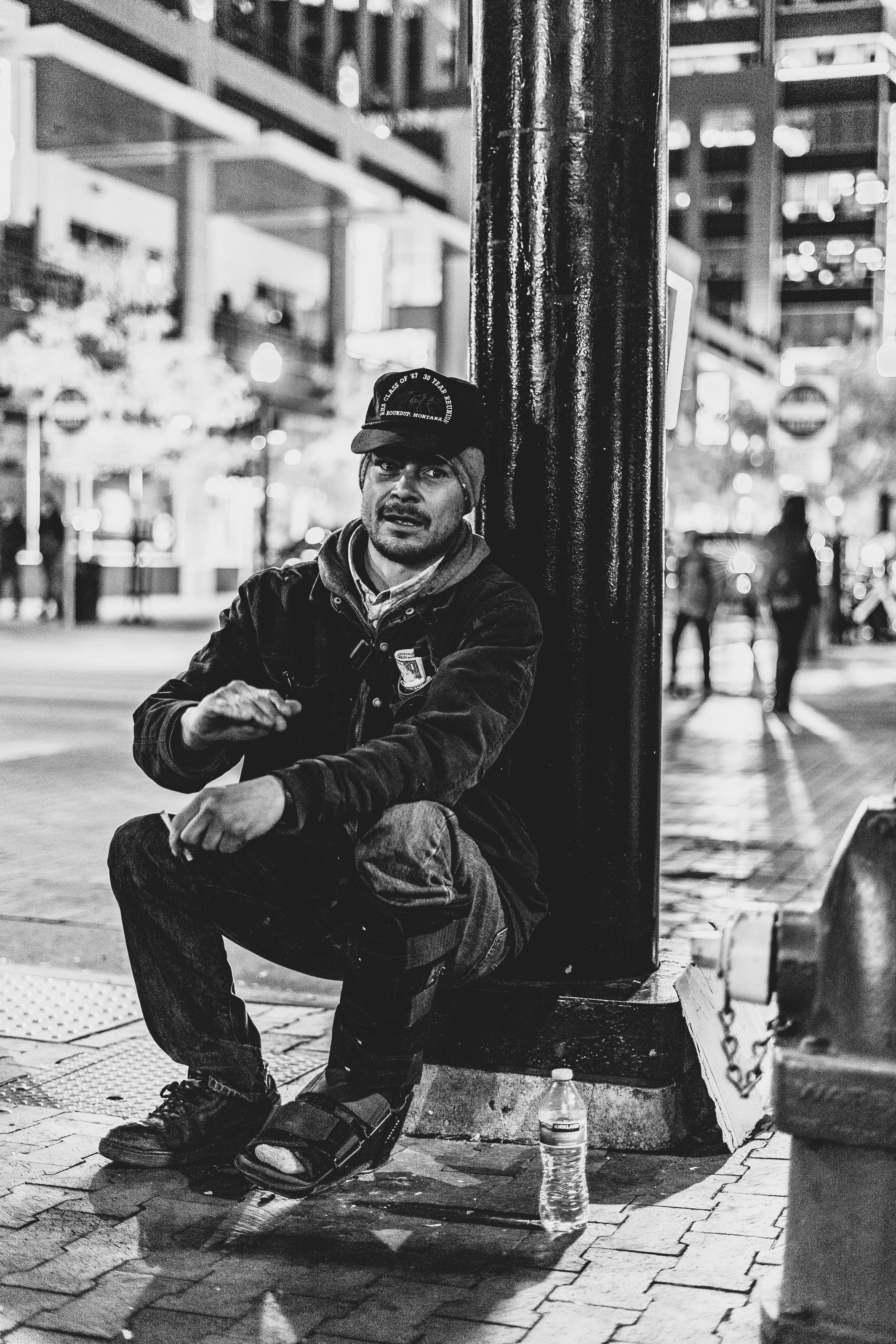 一张黑白城市照片中，一名男子晚上坐在灯柱旁