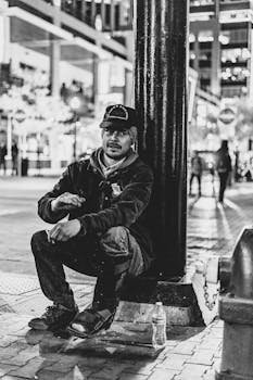 一张黑白城市照片中，一名男子晚上坐在灯柱旁