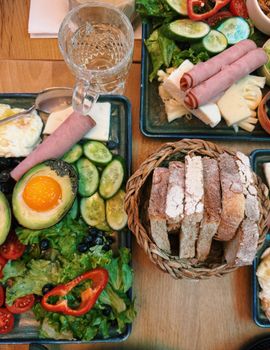 Colorful breakfast spread featuring avocado, bread, ham, cheese, and vegetables.