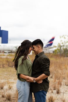 Loving couple in tender embrace outdoors near São Paulo airport with airplane in background.