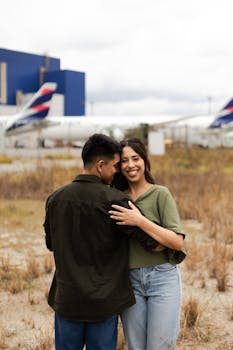 Smiling couple embracing near parked airplanes at São Paulo airport outdoors.