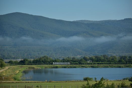 Peaceful view of a serene lake with lush mountains and misty clouds in Romania.