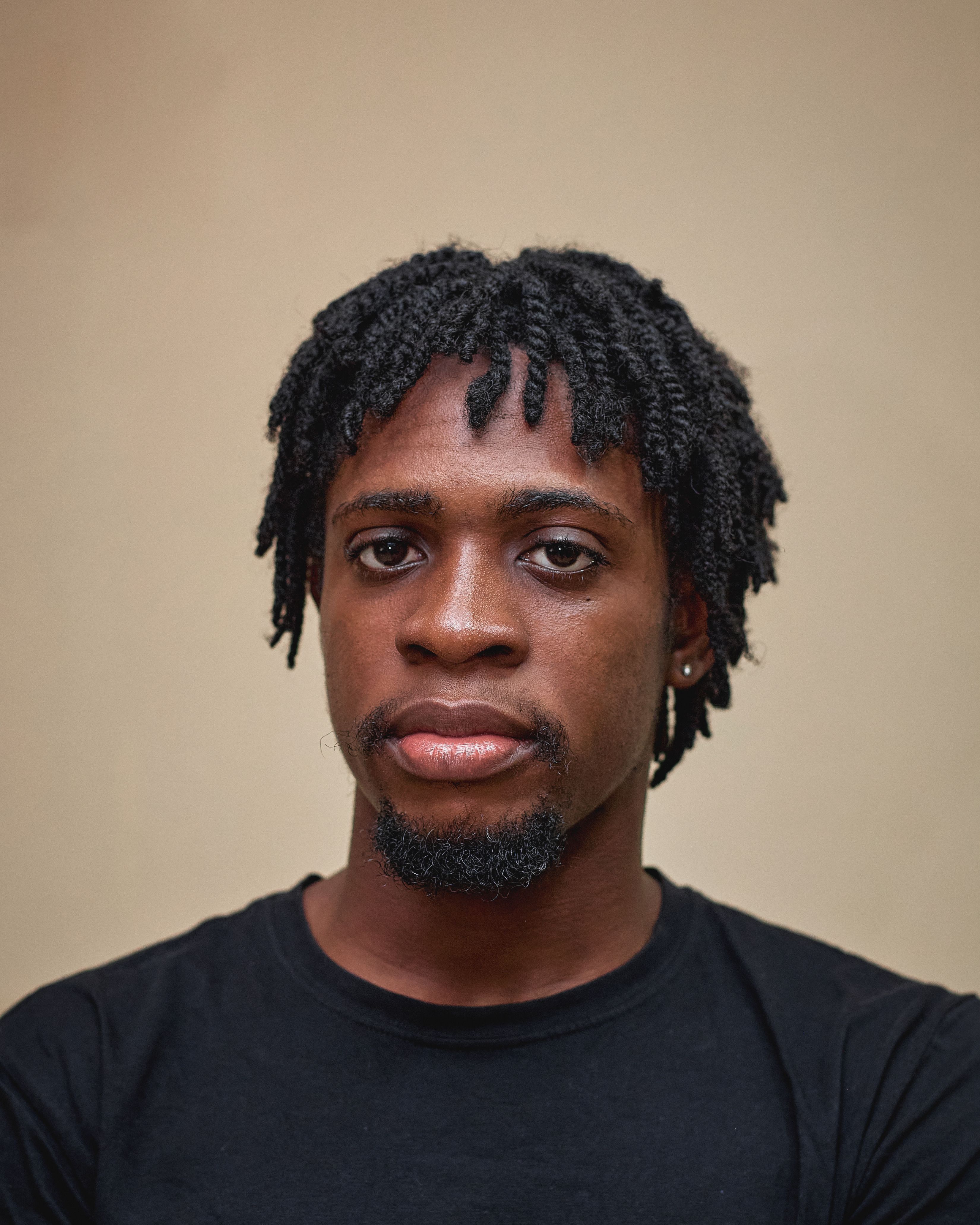 Close-up portrait of a young man with short dreadlocks and facial hair.