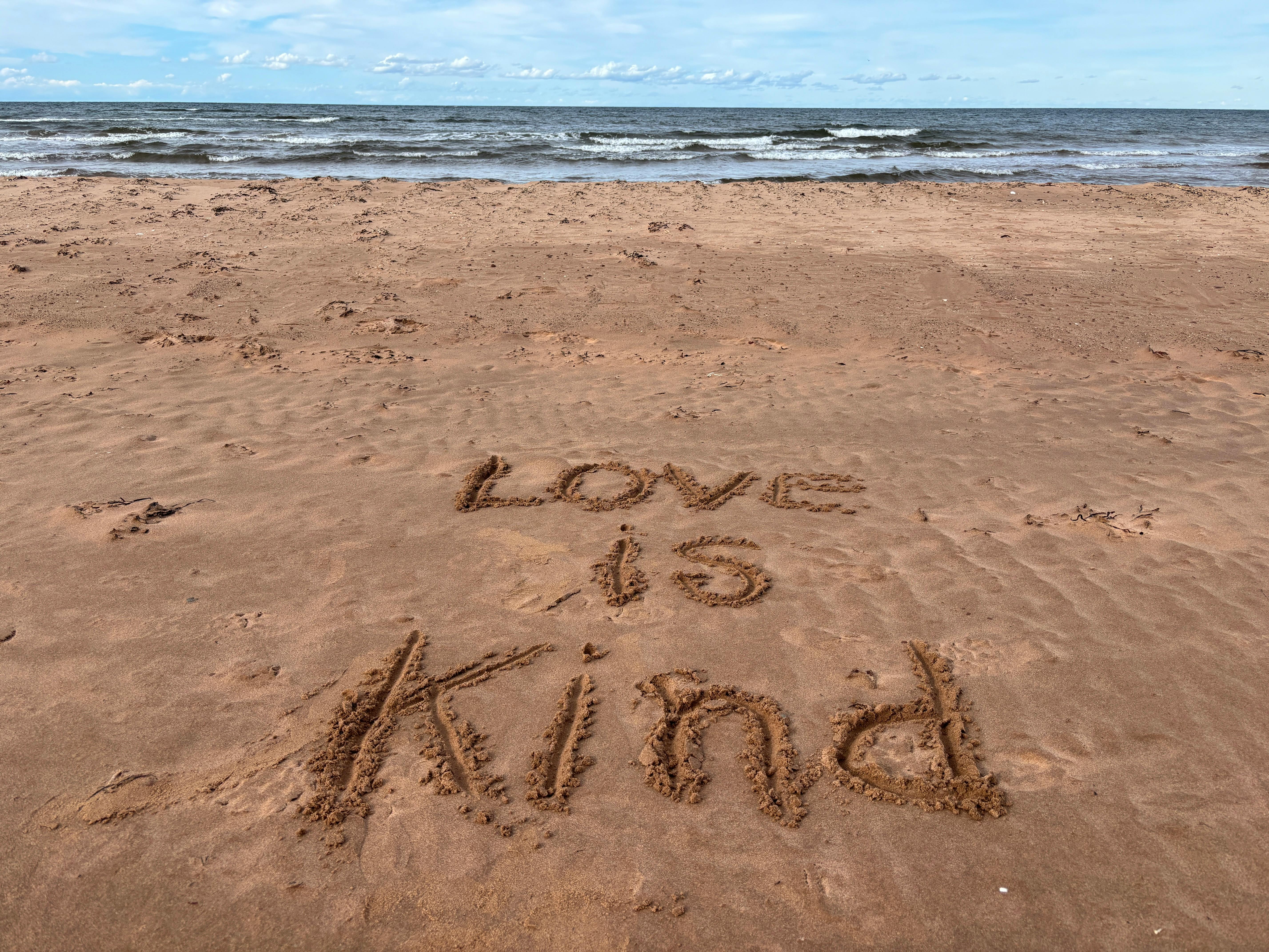 "Love is Kind" written on a beach at Stanhope, conveying positivity and warmth.