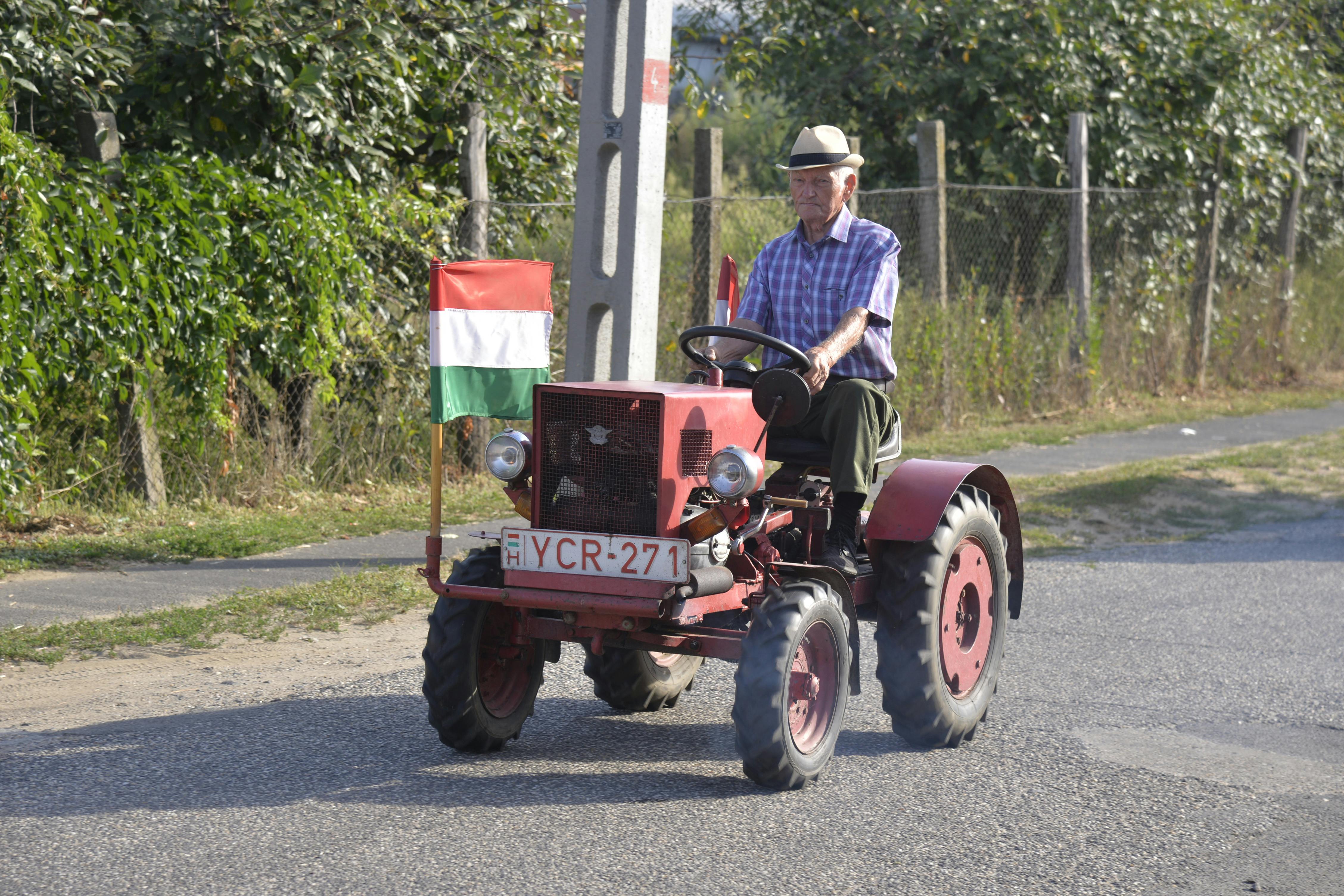 Senior man drives a red vintage tractor with Hungarian flag in Nyírmada.
