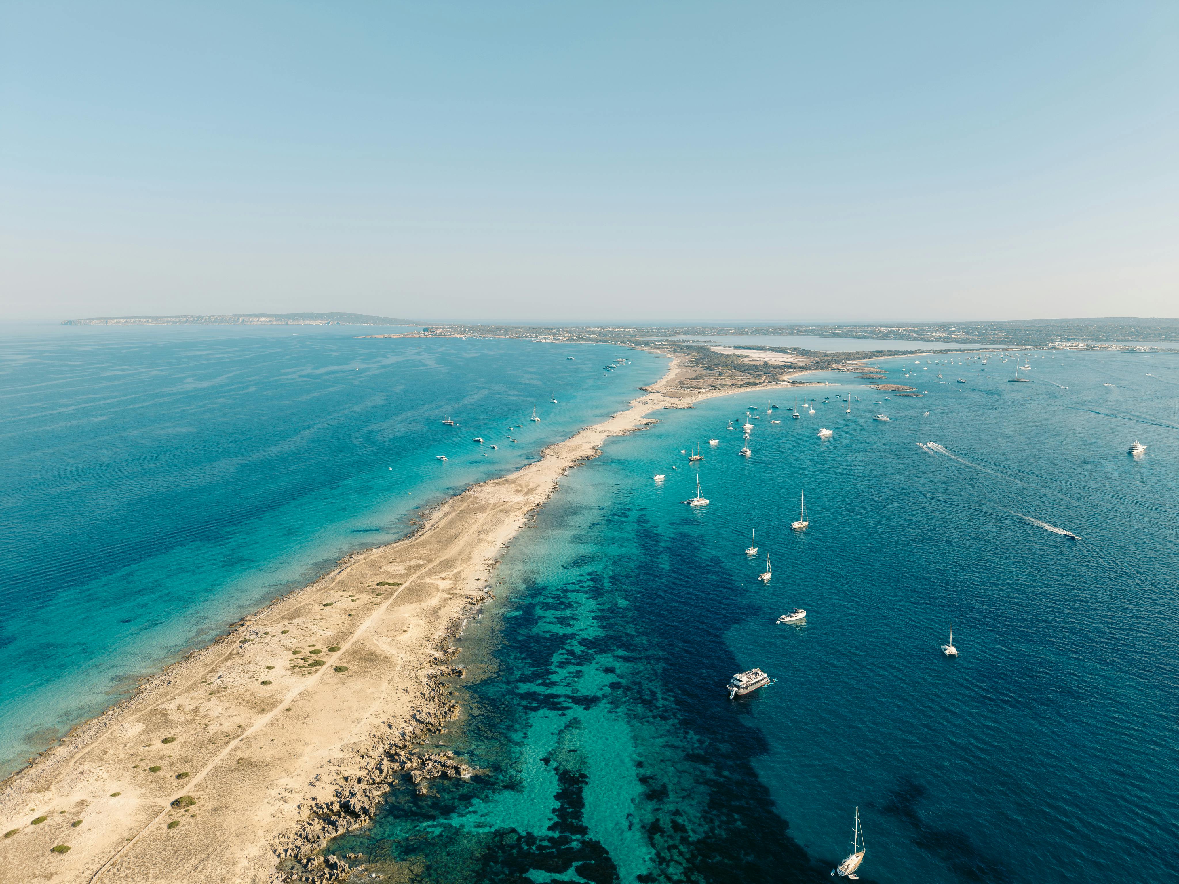 Stunning aerial view of Formentera's coastline with turquoise waters and sailing boats in Balearic Islands, Spain.