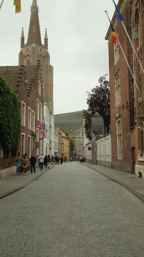 Free Cobblestone street in Bruges with historic buildings and Belfry tower visible. Stock Photo