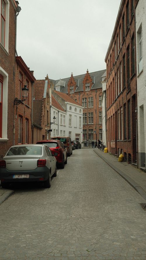 Free Charming cobblestone street lined with parked cars and classic European buildings. Stock Photo