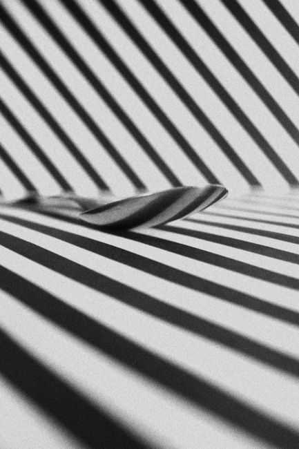 Black and white image of a spoon on a geometric striped surface, playing with light and shadow.