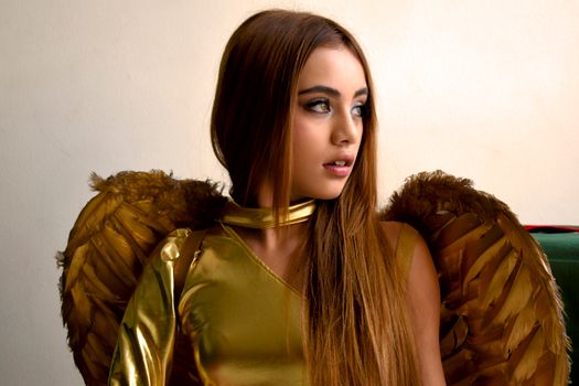 Portrait of young woman in gold angel costume looking to the side.