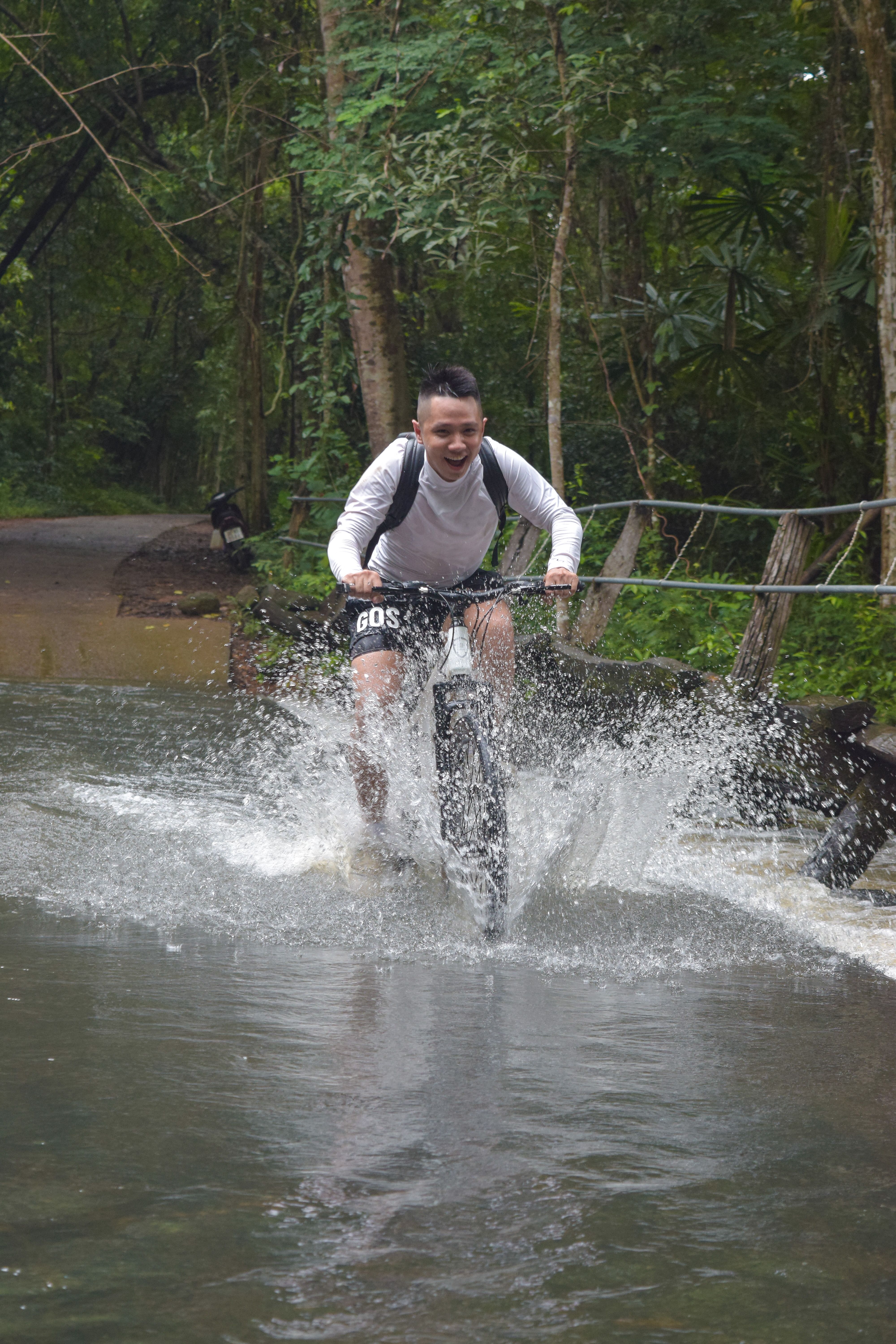 A man riding a bicycle through a forest trail, creating a water splash, showcases outdoor adventure.