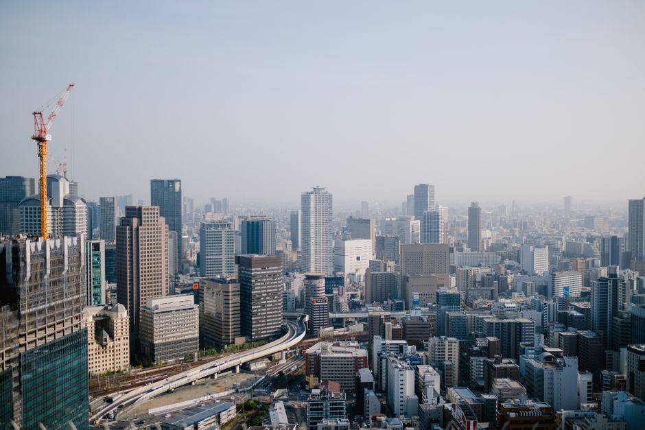 Expansive aerial view of a modern city skyline with skyscrapers and construction cranes.
