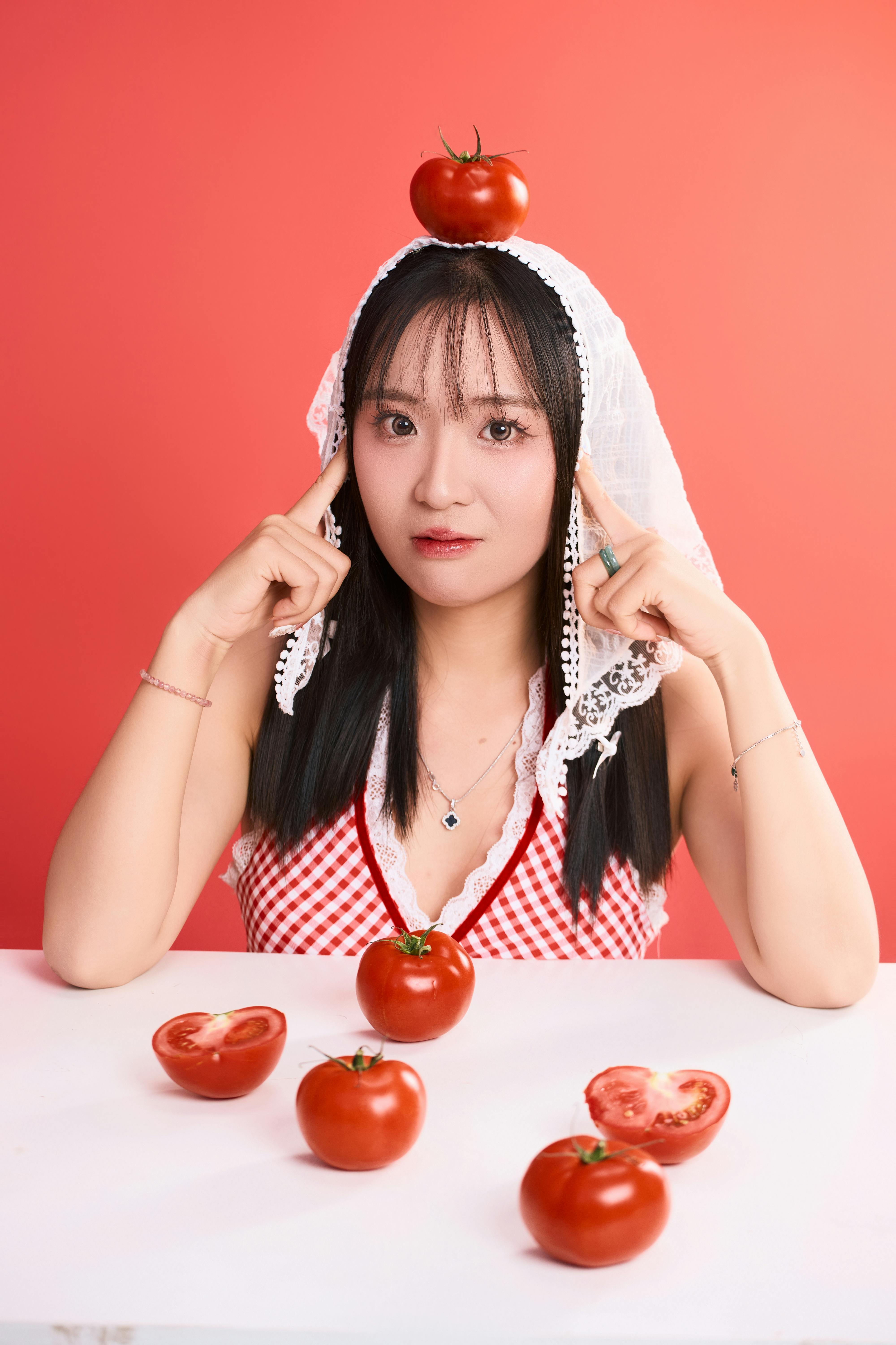 Creative portrait of a woman with tomatoes, highlighting food and fashion on a red backdrop.