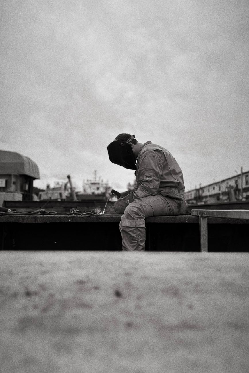 A welder at work in an industrial setting, black and white documentary photograph