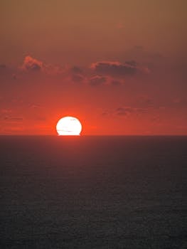 A breathtaking sunrise over the ocean, featuring vivid red and orange hues with scattered clouds.