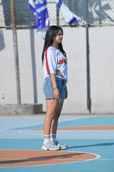 A teenage girl standing on a sunny outdoor basketball court in Bali, Indonesia.