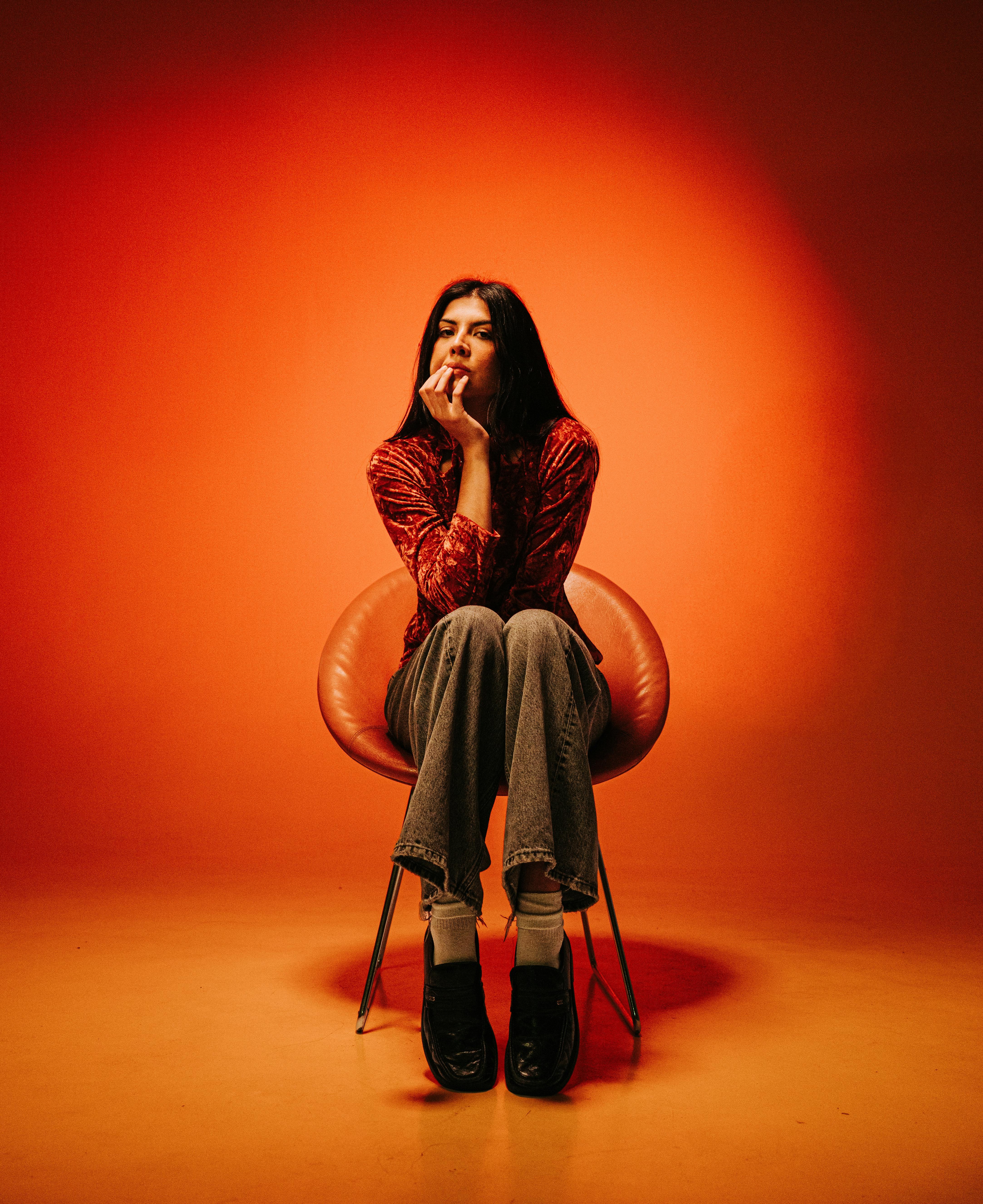 bezplatná Žena v módním oblečení sedí zamyšleně na židli na zářivě červeném pozadí. Základová fotografie