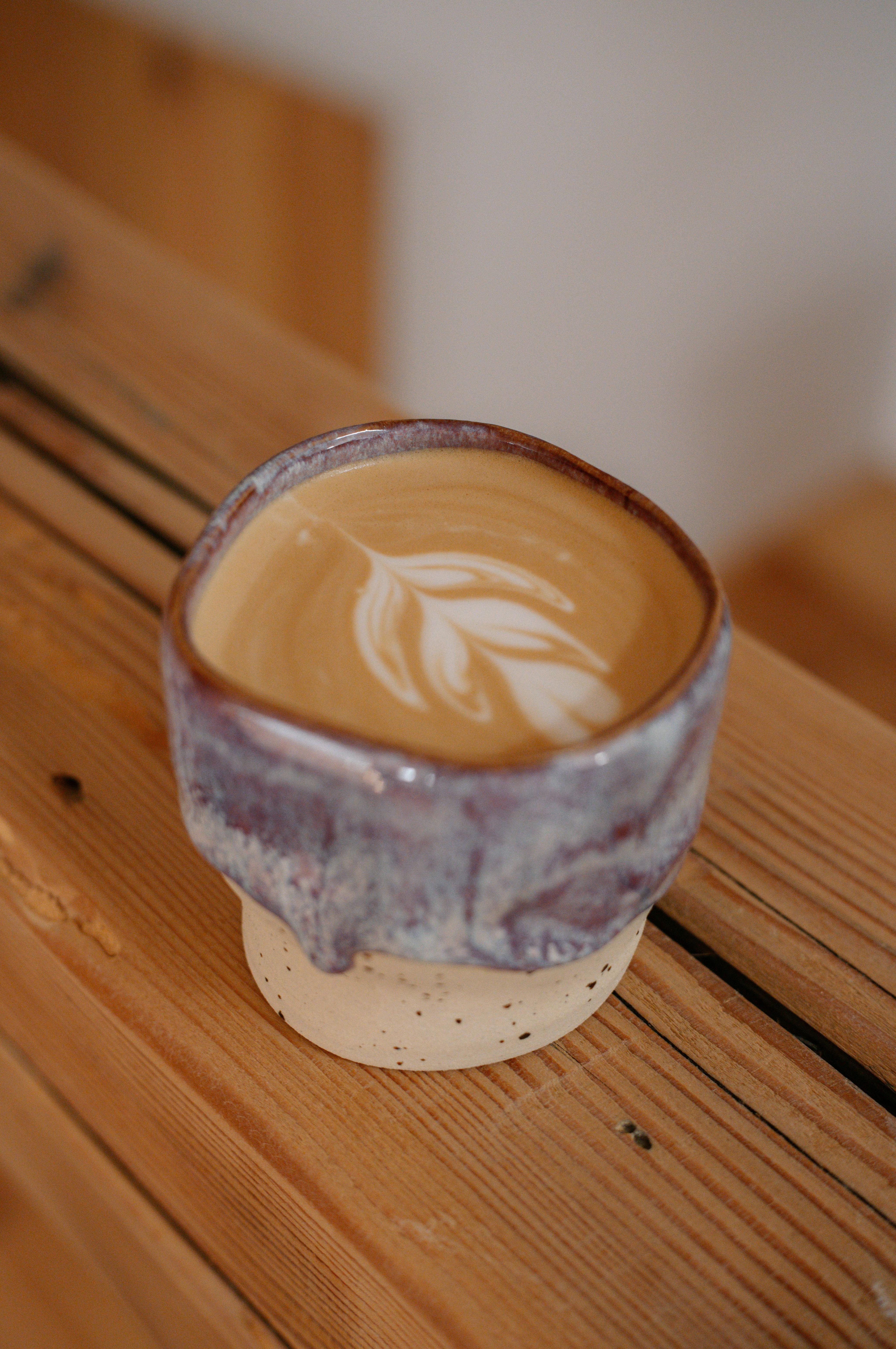 Close-up of a latte with foam art, served in a handmade ceramic mug, on a rustic wooden table.