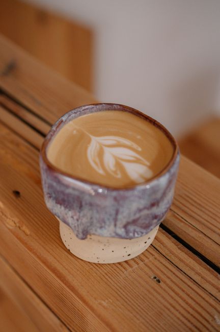 Close-up of a latte with foam art, served in a handmade ceramic mug, on a rustic wooden table.