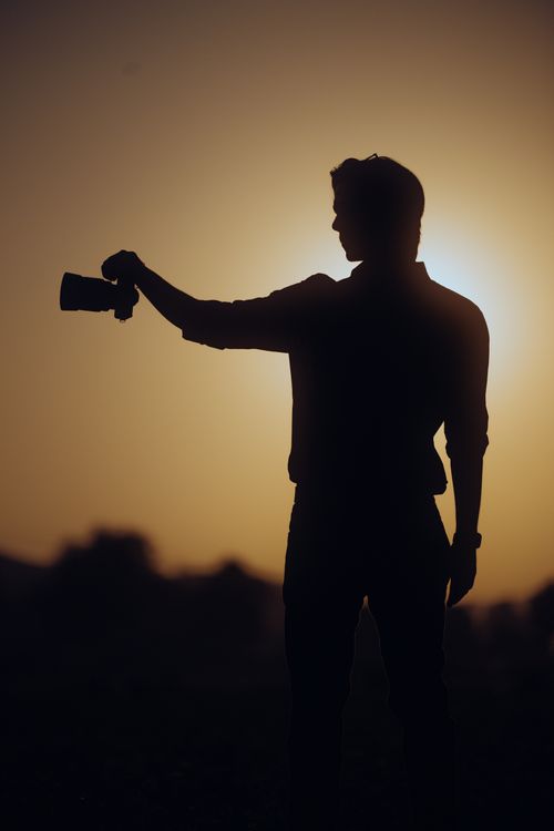 Free A captivating silhouette of a photographer holding a camera against a sunset backdrop, creating a dramatic scene. Stock Photo