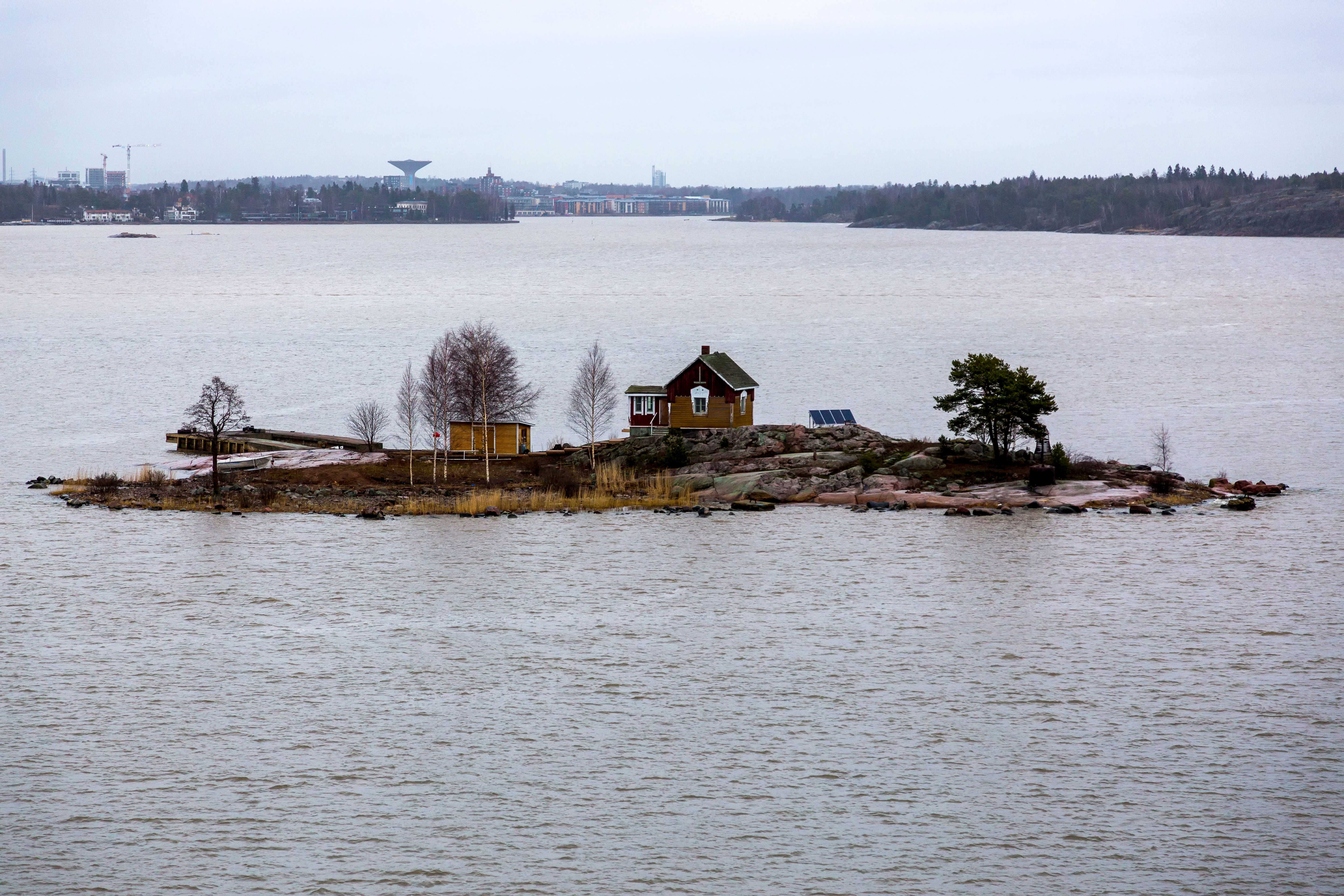 A solitary house on a small island in a serene lake, surrounded by calm waters and an overcast sky.