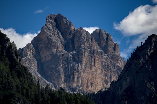 Free A stunning mountain peak rises between lush forests against a clear blue sky. Stock Photo