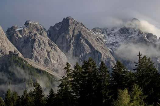 Captivating view of a rugged mountain range with misty clouds and lush pine forest.