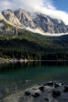 A serene Alpine landscape featuring a clear lake and towering mountains under a bright sky.