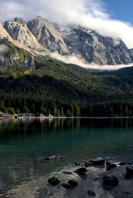 A serene Alpine landscape featuring a clear lake and towering mountains under a bright sky.