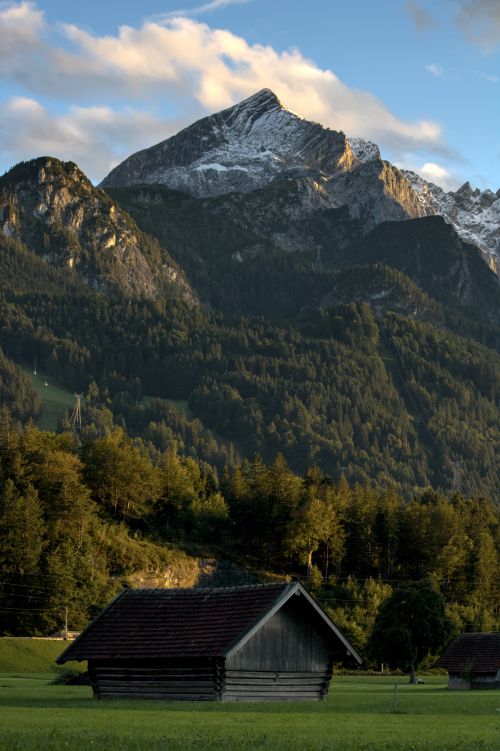 Free Scenic view of an alpine mountain with cabins at sunset, showcasing lush greenery and snow-capped peaks. Stock Photo