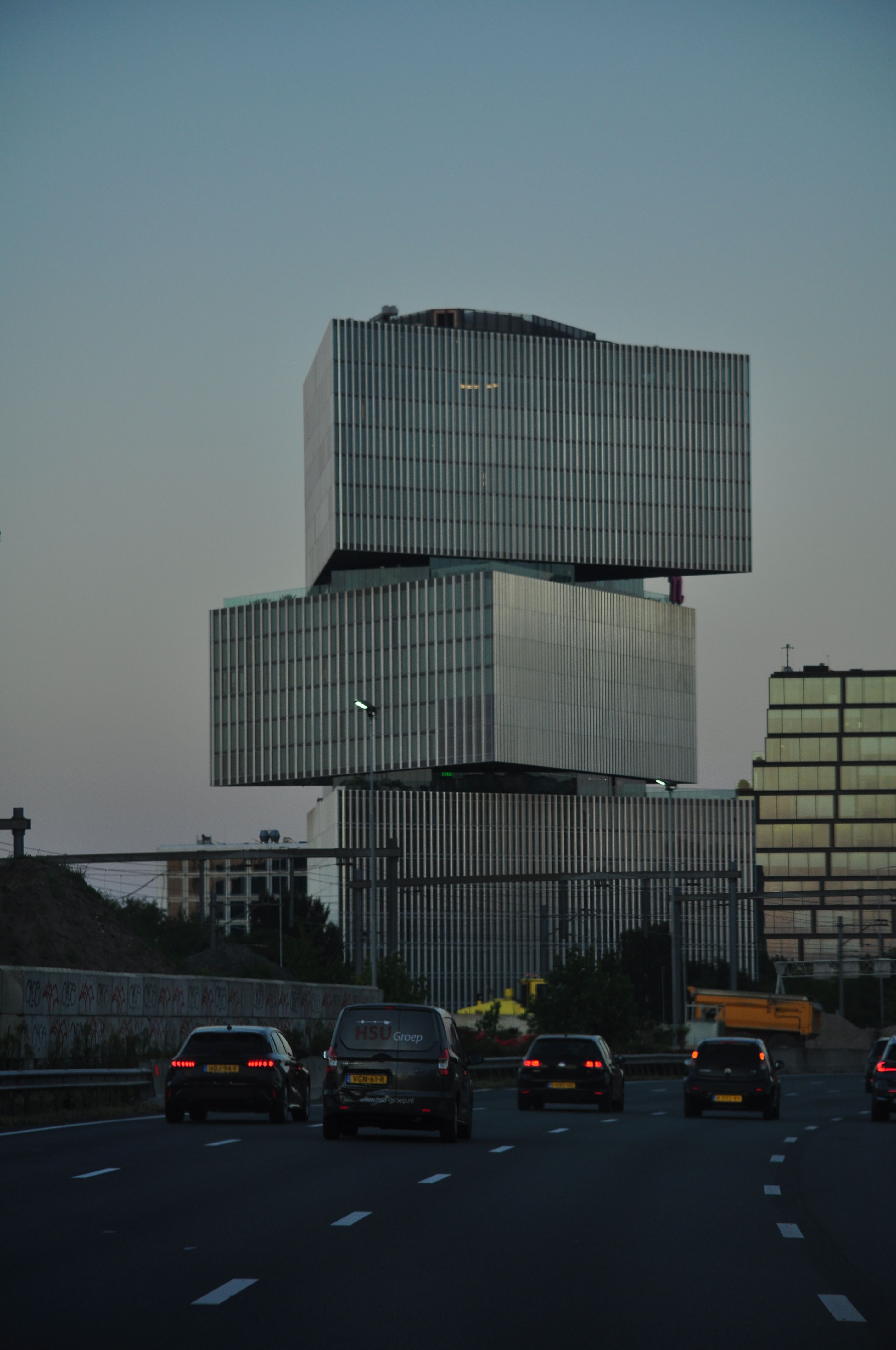 Opvallende moderne architectuur vastgelegd tijdens zonsondergang in Amsterdam, langs een drukke snelweg.