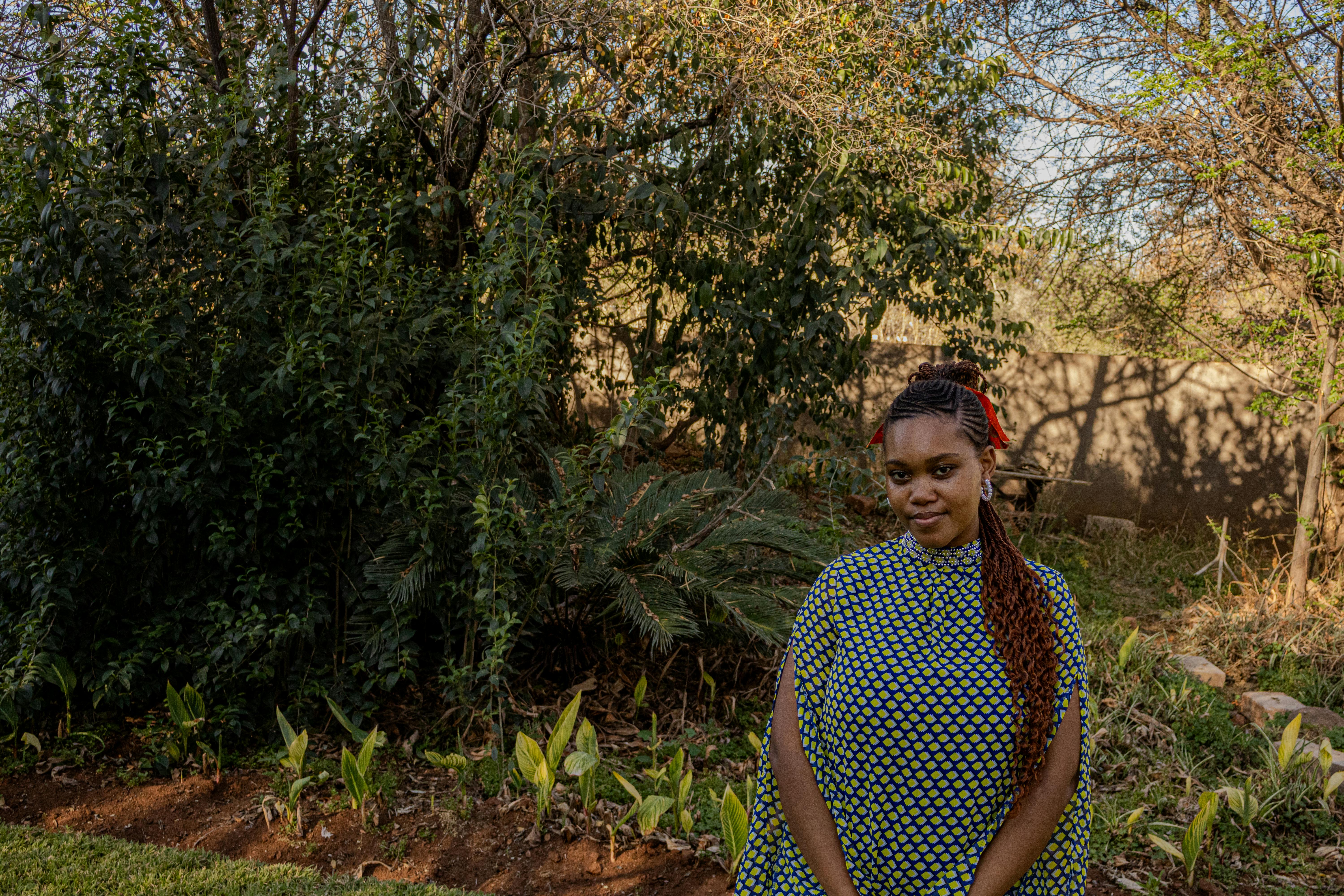 A woman in a patterned outfit stands in a lush green garden, showcasing natural beauty.