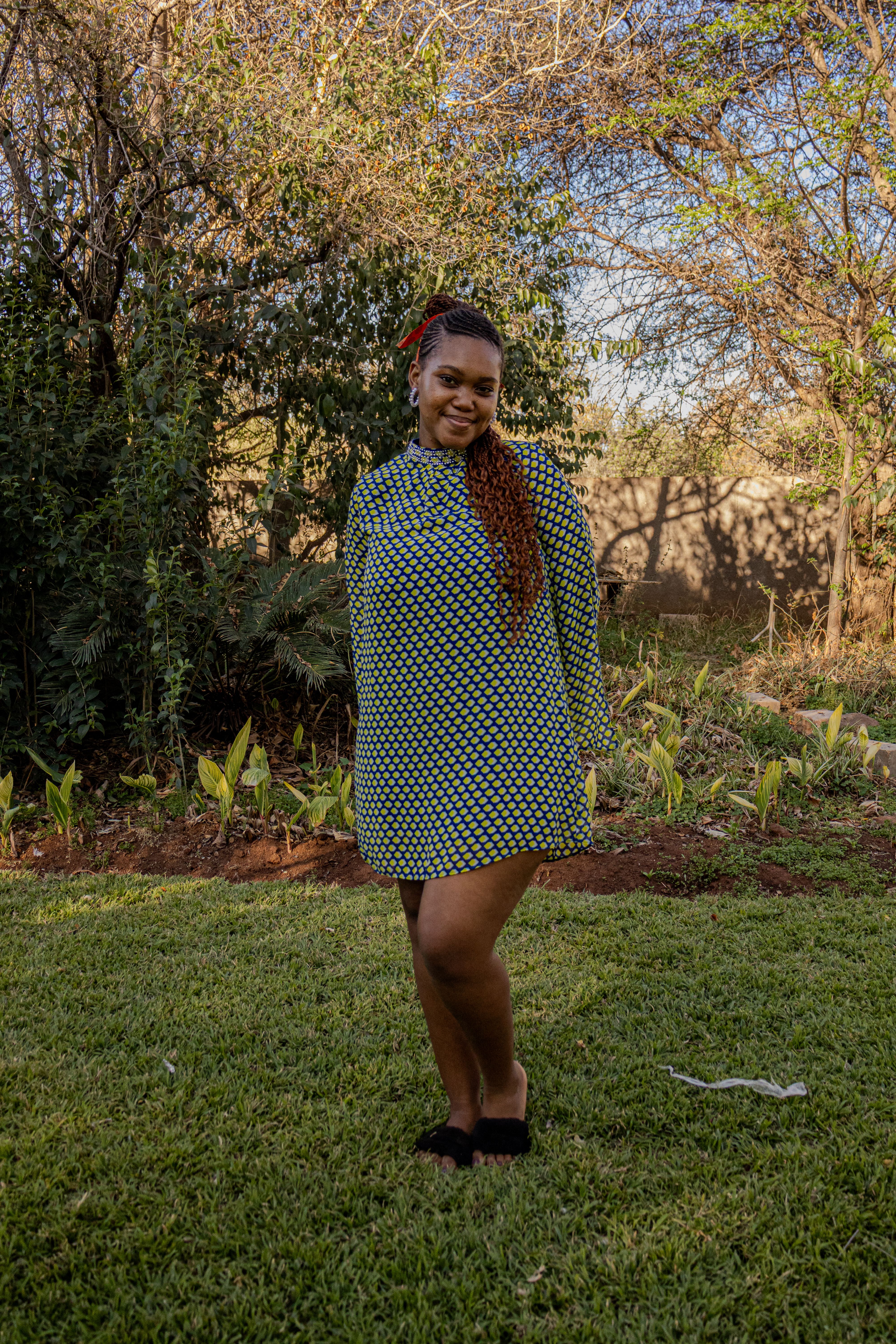 A woman in a green dress smiles while standing on a lawn with trees in the background.