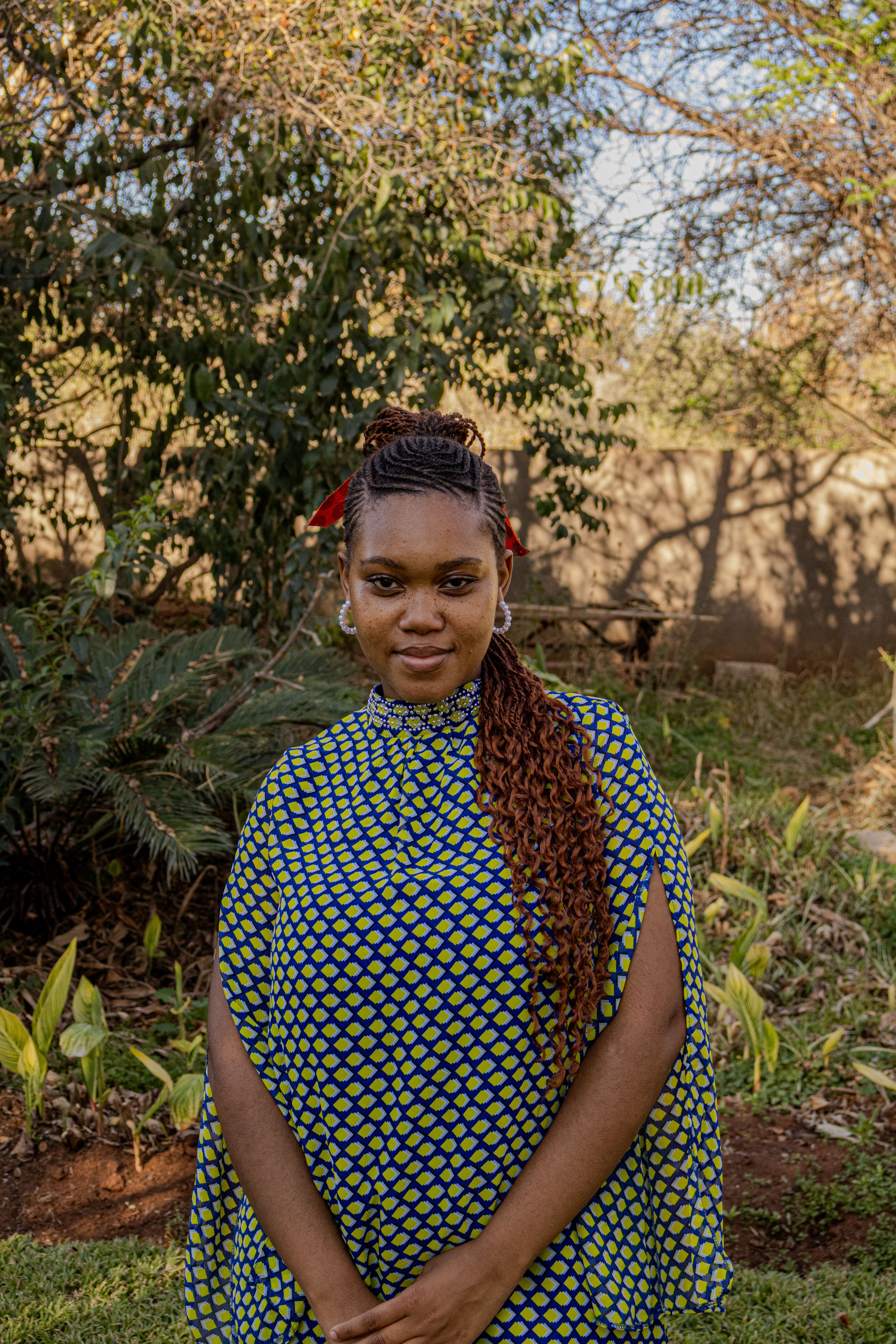 A woman stands confidently in a vibrant dress against a natural outdoor backdrop.