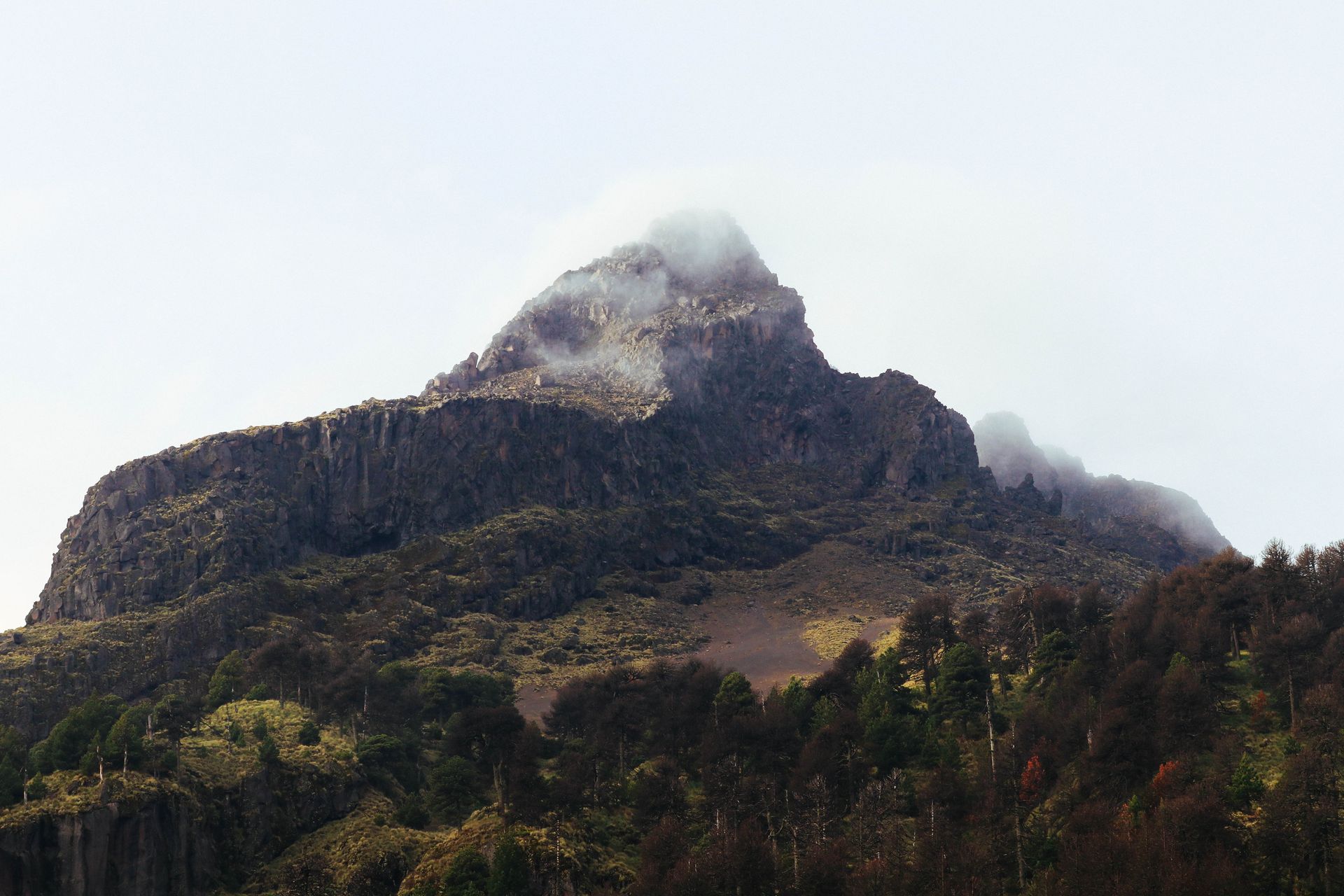 A stunning view of a rugged mountain peak shrouded in mist with lush greenery at the base.
