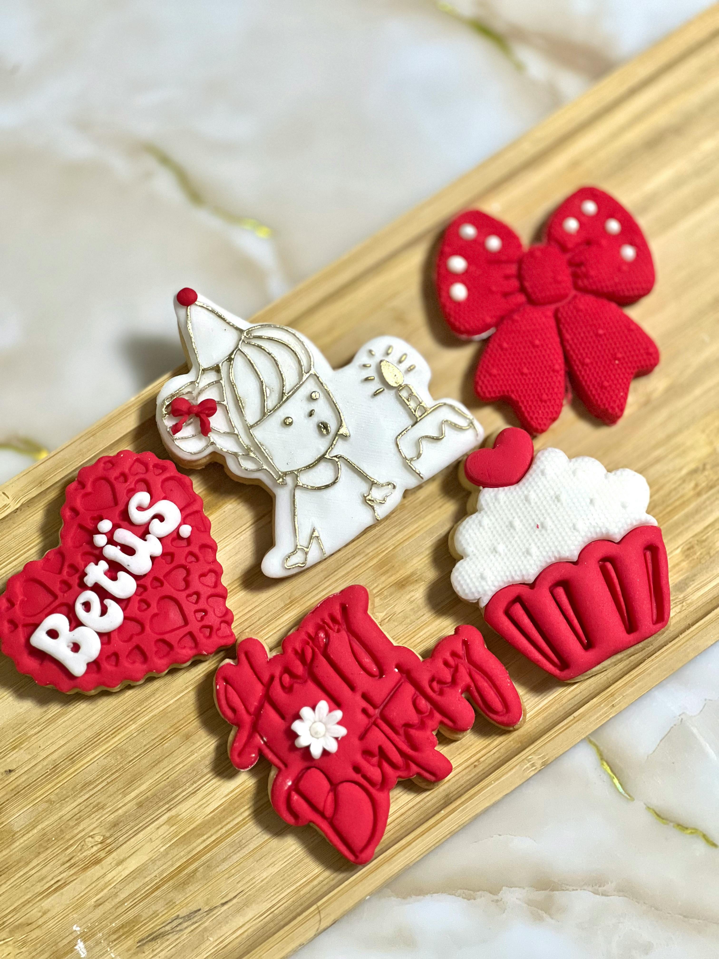 Assorted decorative birthday-themed cookies on a wooden tray in vibrant red and white colors.