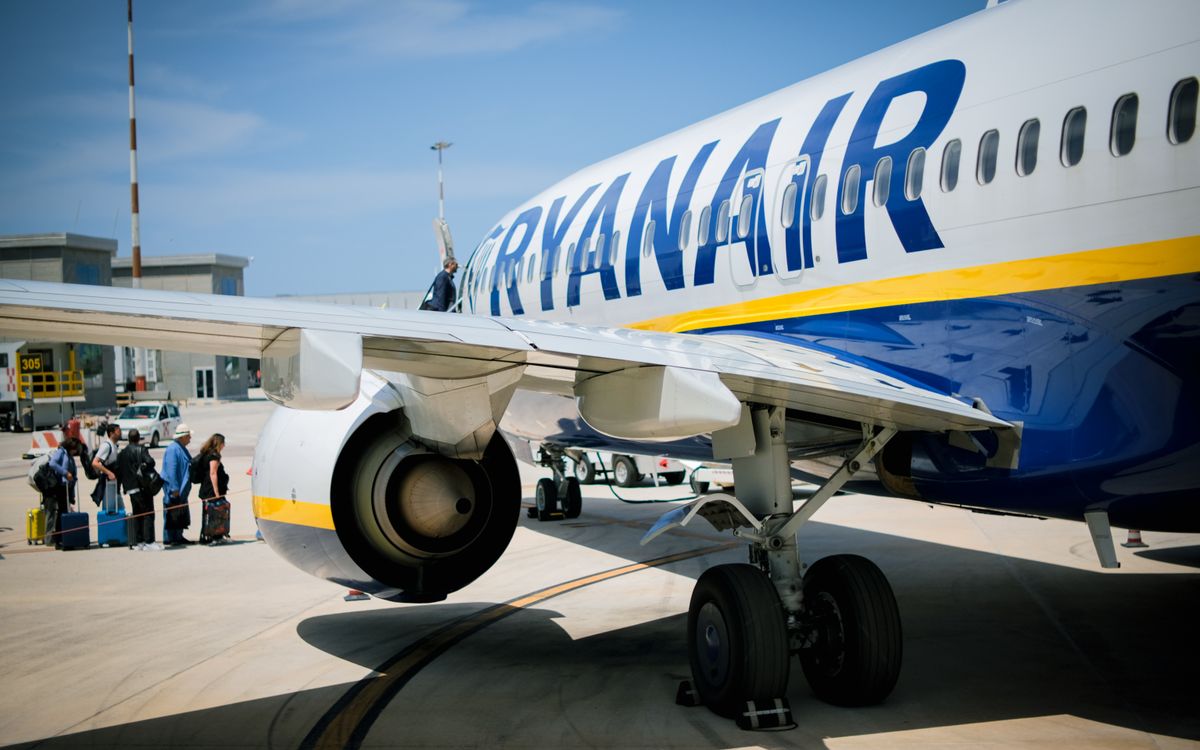 Passengers boarding a Ryanair plane on a sunny day at a Sicilian airport.