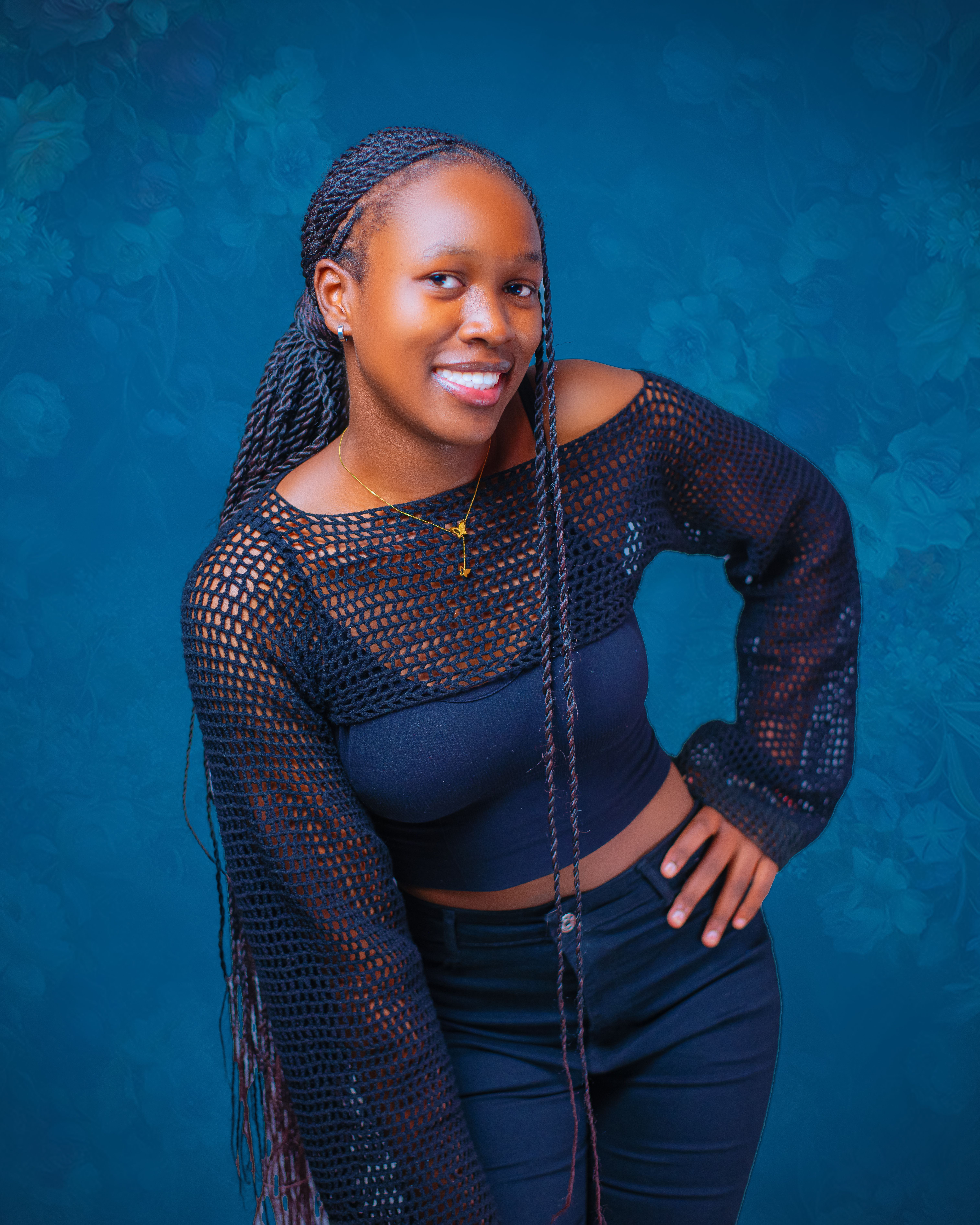 Confident young woman smiling in a stylish black outfit against a blue floral background.