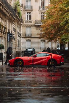 Red sports car parked on a wet Parisian street with fall foliage.