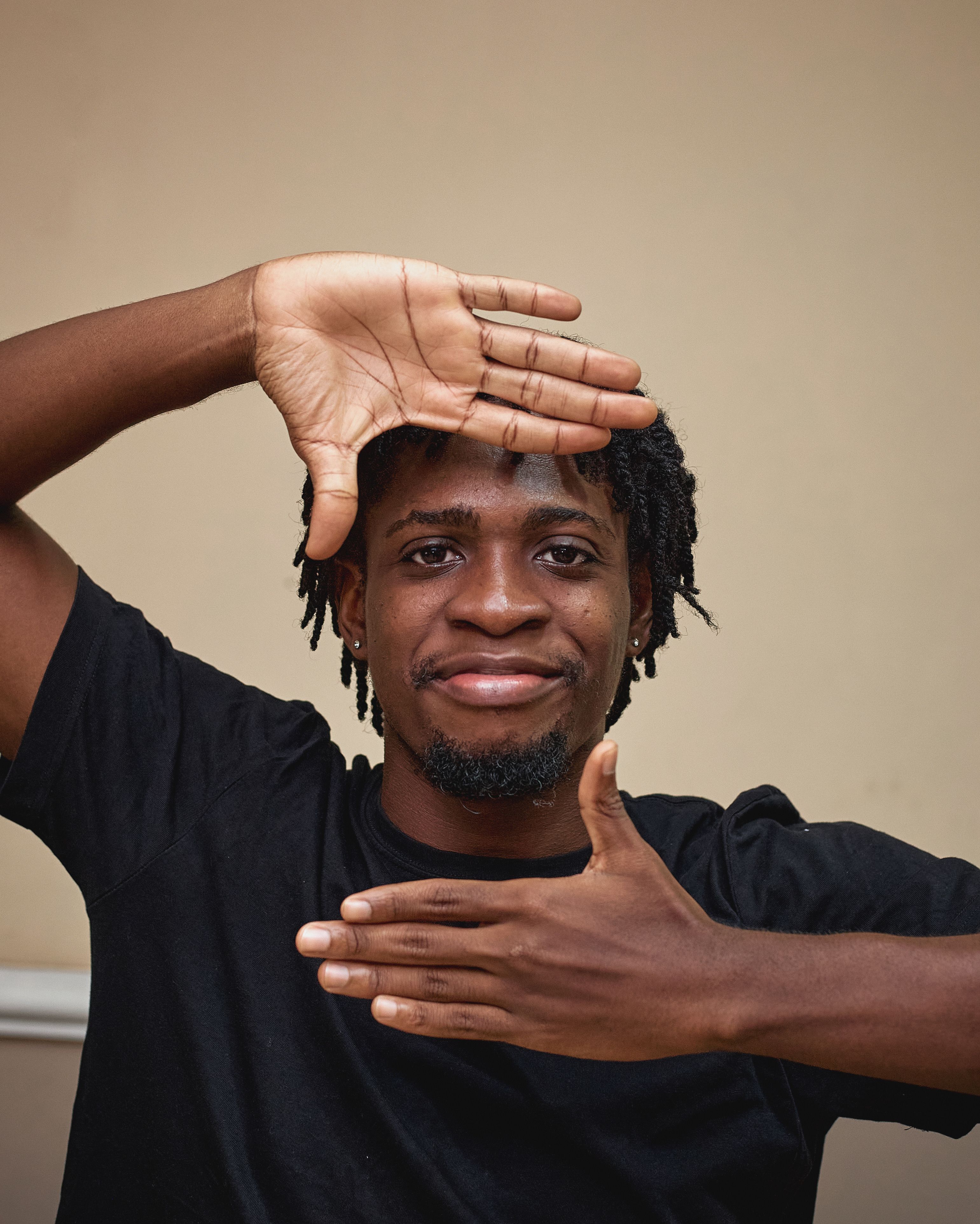 A cheerful man poses indoors, gesturing expressively with his hands.