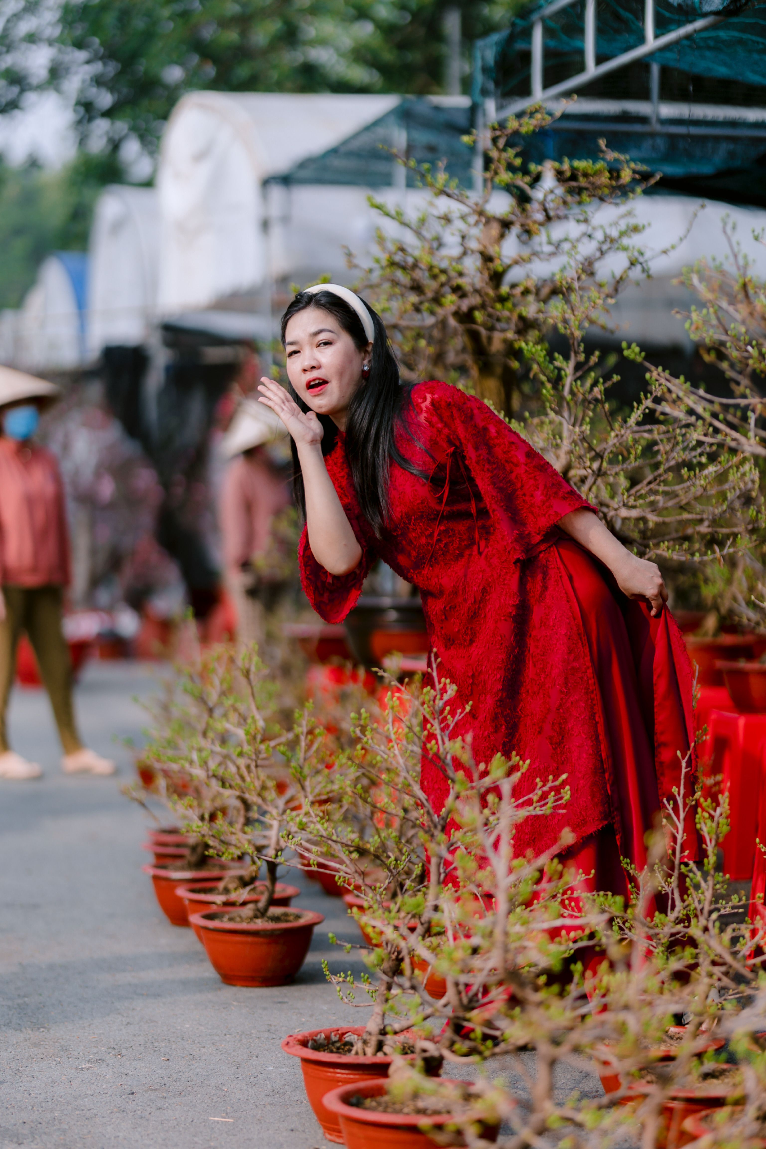Woman wearing a red dress playfully blows a kiss in a vibrant outdoor garden setting.