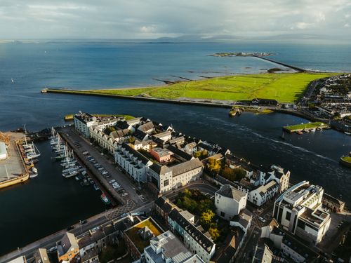 Free Stunning aerial shot of Galway's coastal harbor with vibrant green landscape and blue ocean waters. Stock Photo
