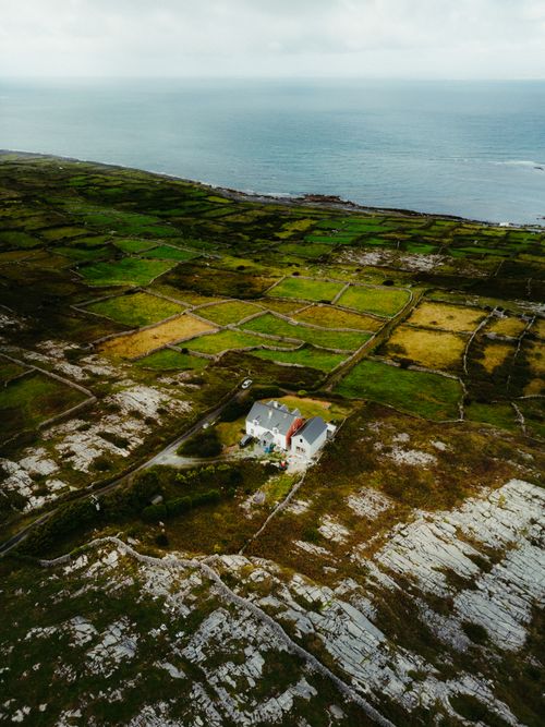 Free Stunning aerial shot of Irish countryside in County Clare, showcasing a lone house amidst green fields and rocky landscape. Stock Photo
