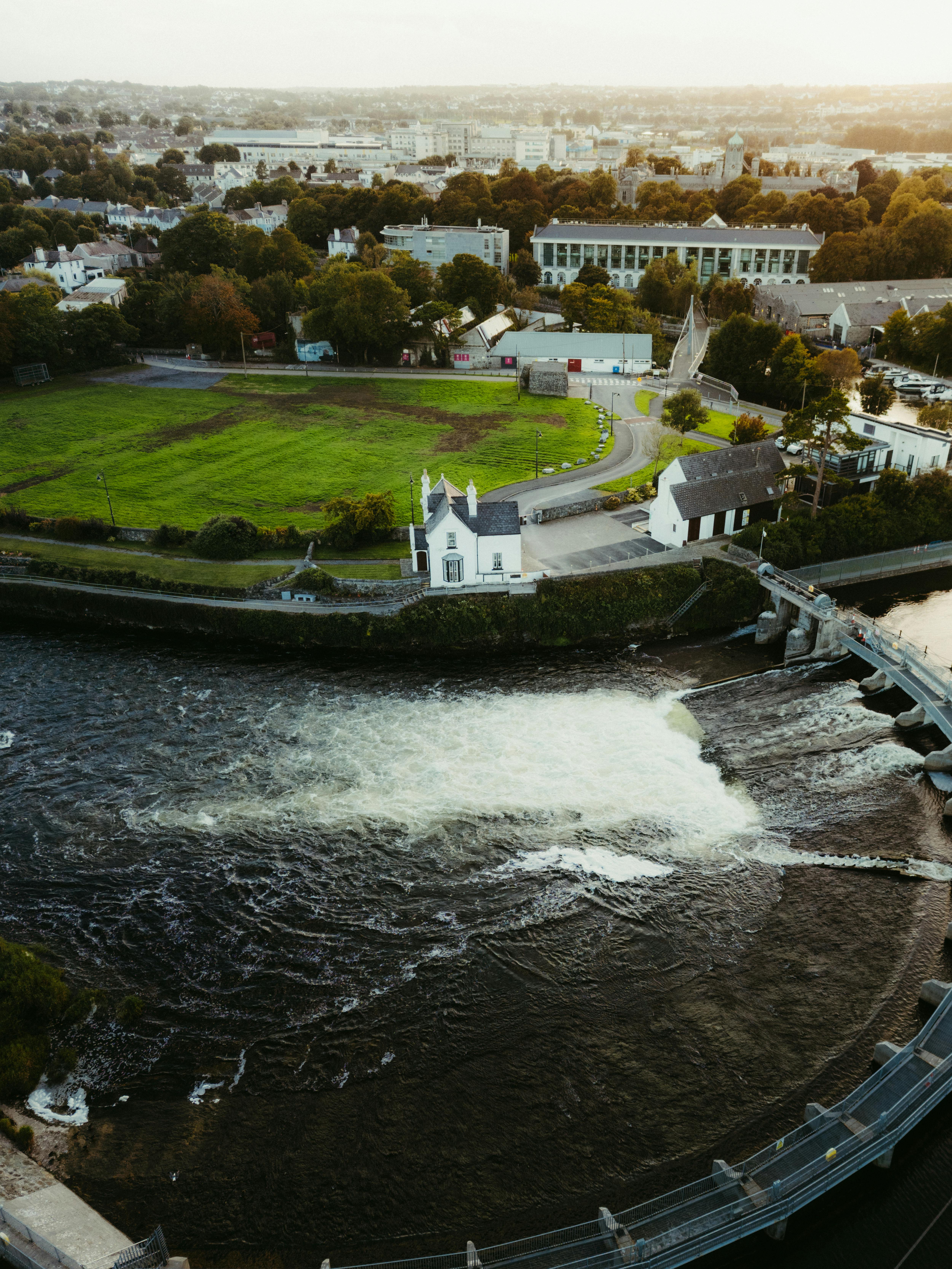 Aerial shot of a river, lush greenery, and buildings in County Clare, Ireland at sunset.